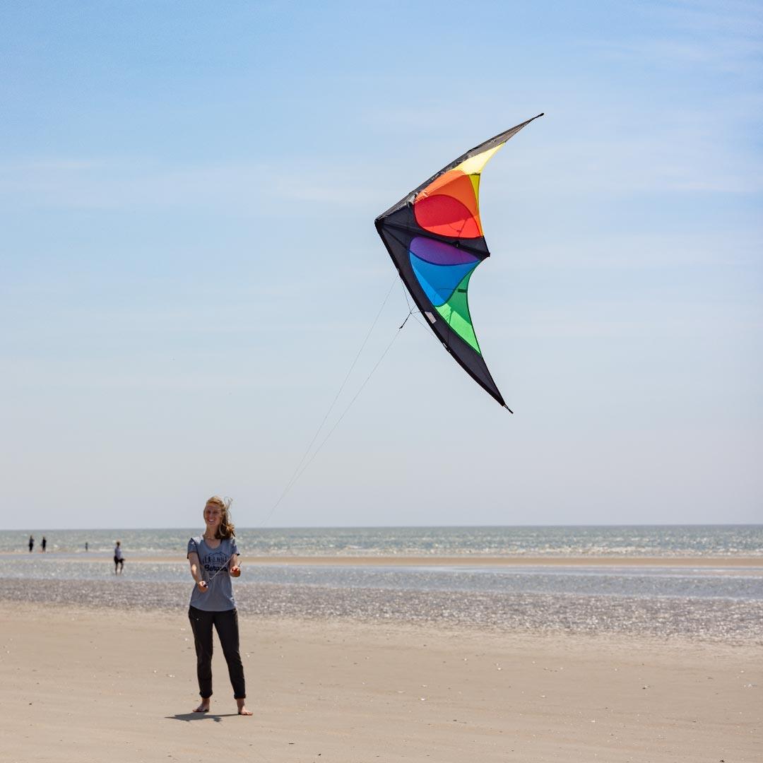 Kvinna som flyger en Bebop sportdrake med färgglada paneler och vitt snöre på en vidsträckt strand