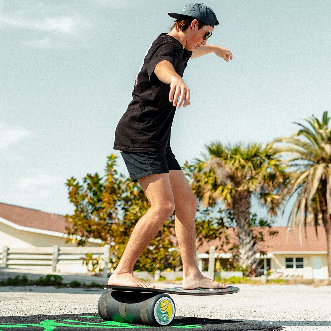 Person i shorts och keps balanserar på en Indoboard med roller på en matta utomhus