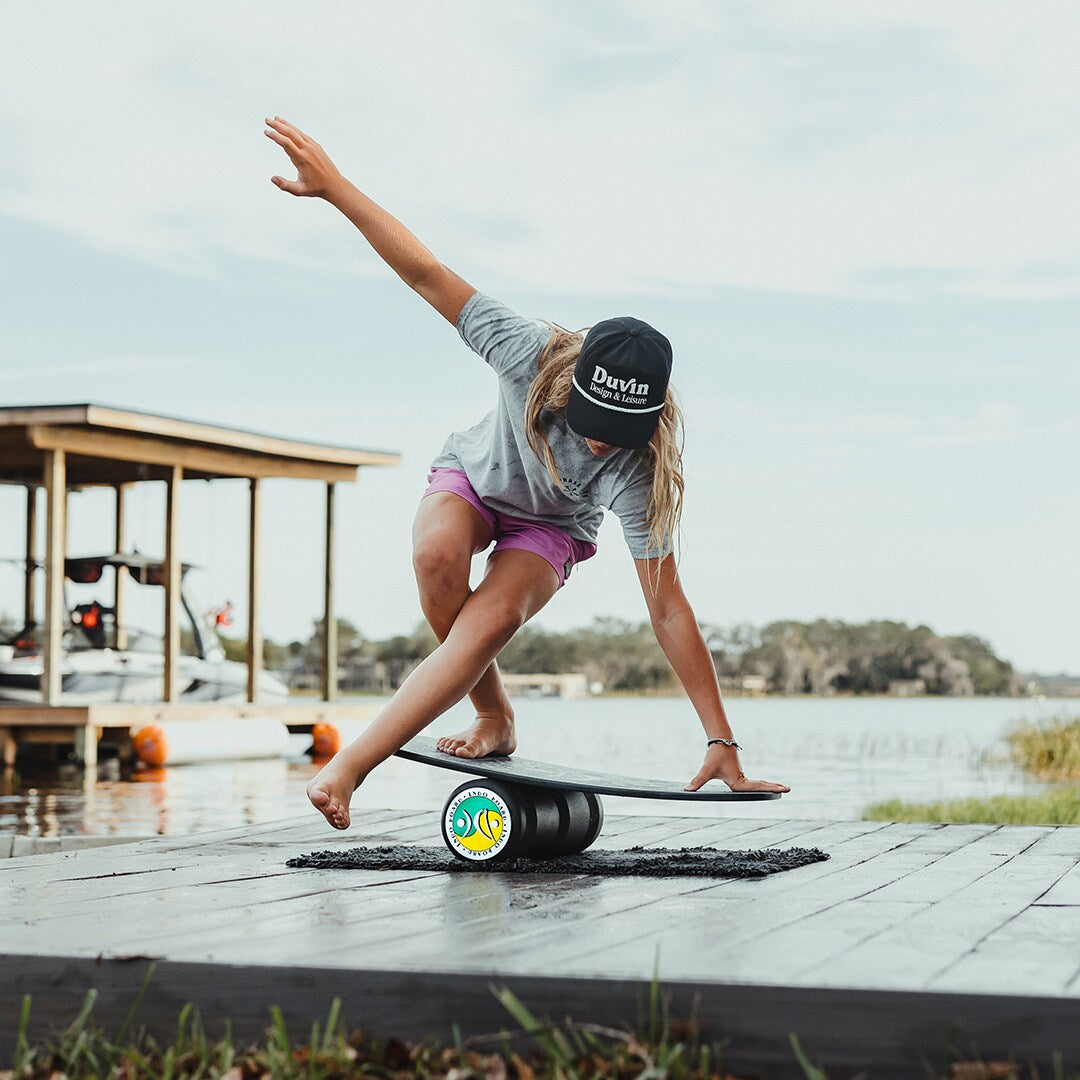 Kvinna i vit t-shirt balanserar på en Indoboard med roller och matta utomhus vid palmer