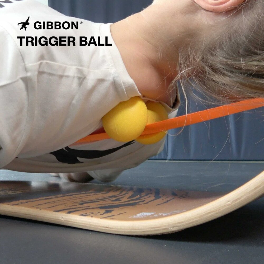 Närbild på en person som ligger på en GIBBON balansbräda och använder två gula GIBBON Trigger Balls för att punktmarkera muskelmassage vid nacke och axlar.