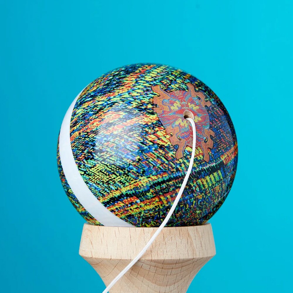 Närbild på bollen till en KROM Noia 5 kendama med ett konstnärligt mönster i blått, gult och rött samt ett vitt snöre mot en turkos bakgrund
