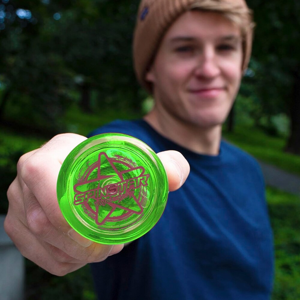En ung man håller fram en genomskinlig grön Spinstar yoyo från YoyoFactory mot kameran utomhus