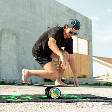 Man balanserar i en låg surf-ställning på en Rockerboard med roller och matta utomhus