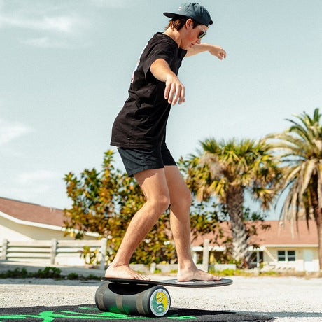 Person i shorts och keps balanserar på en Indoboard med roller på en matta utomhus