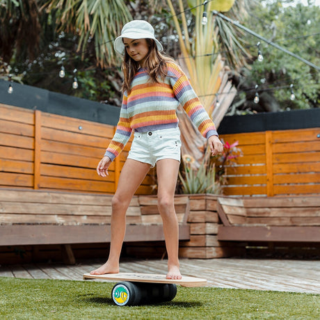 Flicka i stråhatt balanserar på en Indoboard med roller på en gräsmatta