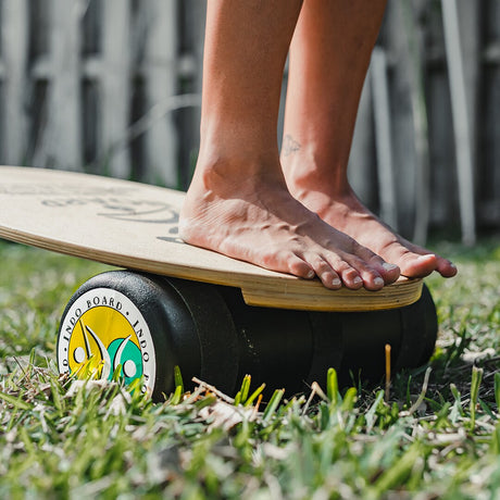 Närbild på fötter som balanserar barfota på Indoboard balansbräda med roller på gräs