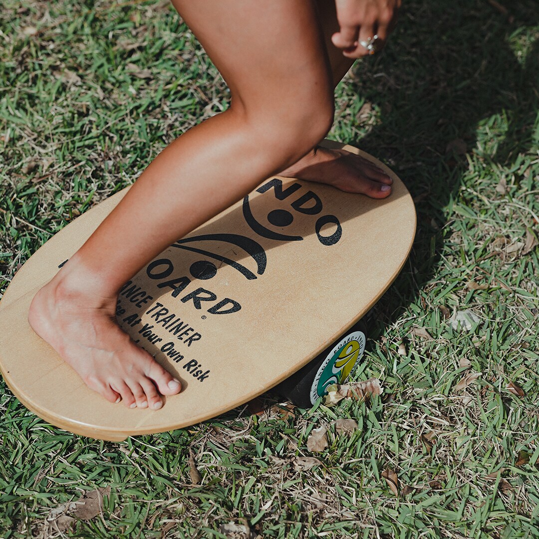Närbild på fötter som balanserar barfota på en Indoboard balansbräda med roller på gräs