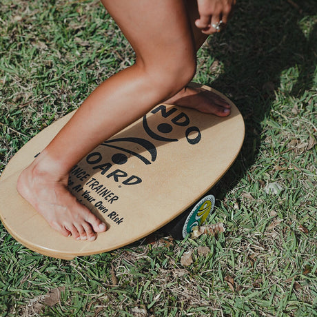 Närbild på fötter som balanserar barfota på en Indoboard balansbräda med roller på gräs