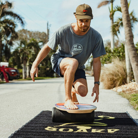 Man balanserar i en låg ställning på en Indoboard med roller på en matta utomhus