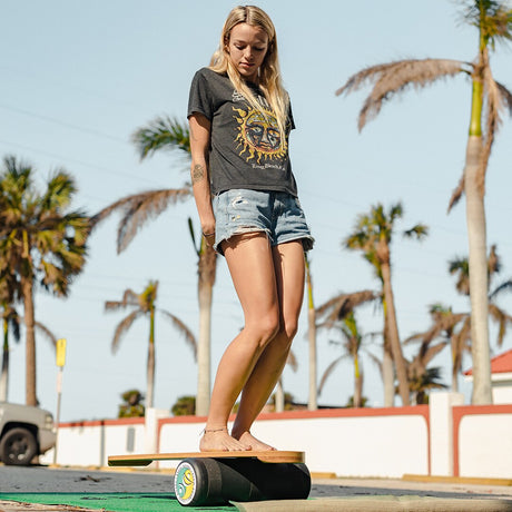 Kvinna i shorts balanserar stående på en Indoboard med roller utomhus vid palmer