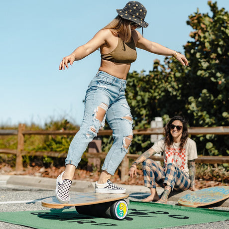 Kvinna i jeans balanserar på en Indoboard med roller och matta utomhus under instruktion