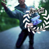 Actionbild där en lila och blå Arrow Galaxy jojo är i fokus och snurrar på ett neongrönt snöre. I bakgrunden syns konturerna av en person i en hoodie på en väg omgiven av grönska. Bilden har vit grafik med logotyperna för "Arrow Elite" och "YoyoFactory"