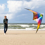 En kvinna som flyger en färgstark, mönstrad styrbar drake på en sandstrand vid havet.