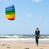 Gemini sa En kvinna som flyger en regnbågsfärgad Symphony-drake på en sandstrand vid havet en solig dag.