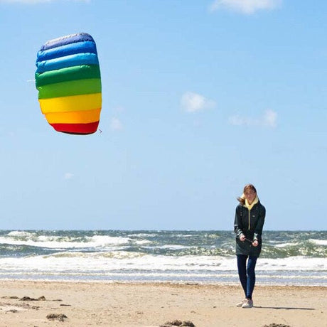Gemini sa En kvinna som flyger en regnbågsfärgad Symphony-drake på en sandstrand vid havet en solig dag.