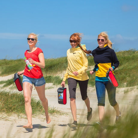 Tre personer som springer skrattande längs en sandstrand bärandes på varsin röd väska innehållande en Symphony Beach III-drake