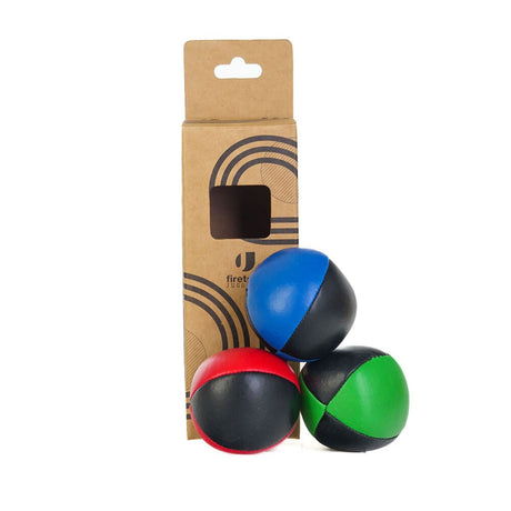 Tre Firetoys jongleringsbollar i kombinationerna röd/svart, blå/svart och grön/svart, fotograferade framför sin bruna kartongförpackning