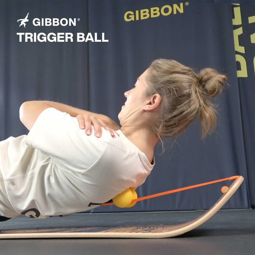 Kvinna som ligger på en GIBBON balansbräda och använder en gul GIBBON Trigger Ball för att massera ryggen under ett träningspass