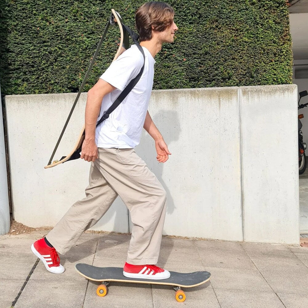 En man som åker skateboard på en trottoar med en GIBBOARD smidigt buren över axeln med en svart GIBBON Shoulderstrap