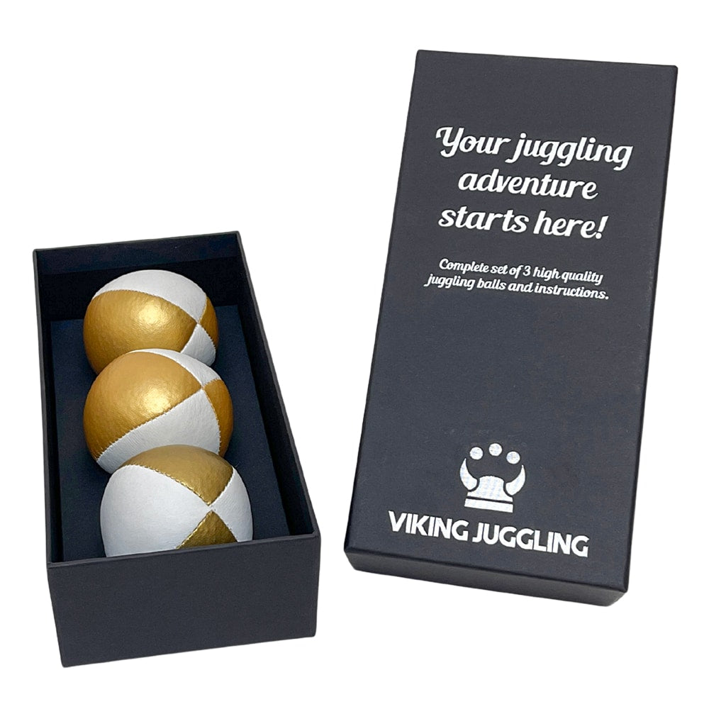 Ett set med tre guld-vita 4-panel jongleringsbollar i konstläder, presenterade i en svart presentask från Viking Juggling.