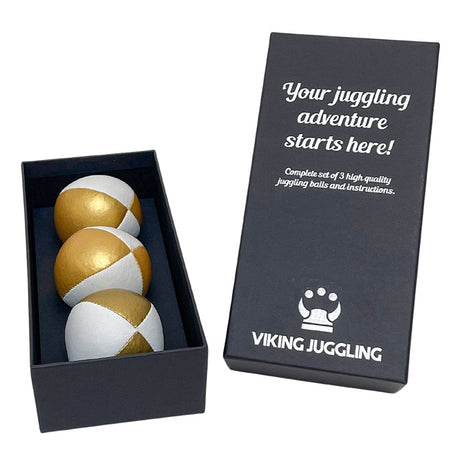 Ett set med tre guld-vita 4-panel jongleringsbollar i konstläder, presenterade i en svart presentask från Viking Juggling.