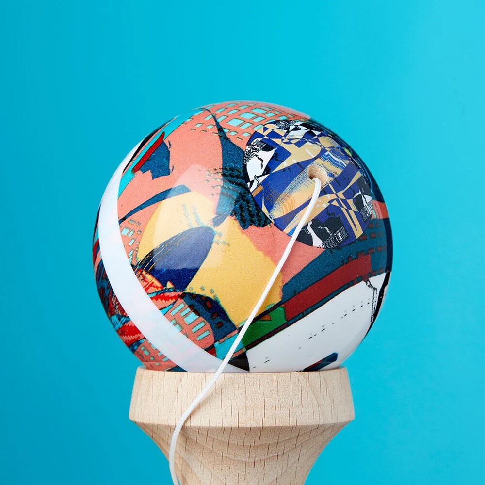 Närbild på bollen till en KROM Noia 4 kendama med ett konstnärligt mönster i blått, orange och gult samt ett vitt snöre mot en turkos bakgrund