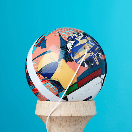 Närbild på bollen till en KROM Noia 4 kendama med ett konstnärligt mönster i blått, orange och gult samt ett vitt snöre mot en turkos bakgrund