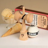 KROM Strogo Neapolitan kendama i ljust trä uppställd bredvid sin temaförpackning tillsammans med en glasskål med vaniljglass och en tom glasstrut på en vit yta.