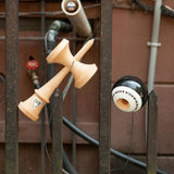 KROM Pop LOL kendama i ljust bokträ med en svart och vit boll (tama) samt svart snöre hängande på ett mörkt metallstaket utomhus