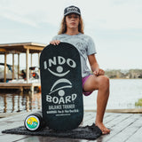 Indo Board Rockerboard i svart med vit logotyp hålls av en person som sitter på en brygga. Visar den svarta rullen och en liten matta