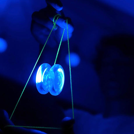 En genomskinlig blå jojo med inbyggd LED-belysning som lyser starkt hänger i ett neongrönt snöre i ett mörkt rum där konturerna av en person syns i bakgrunden