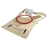 Tualoop-set bestående av en röd ring, fyra kontrollpinnar i trä och en instruktionsmanual liggande på en beige tygpåse med Tualoop-logotypen.