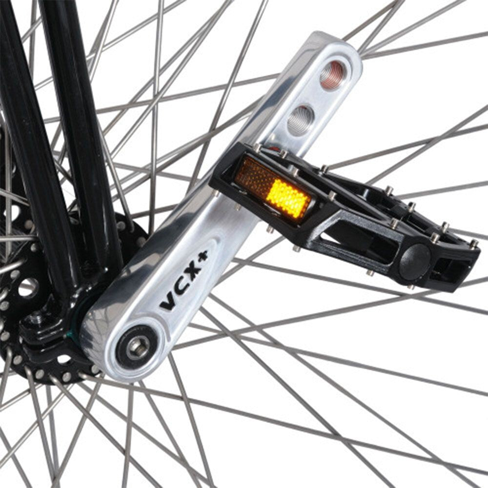 Närbild på den polerade Nimbus VCX Plus-vevarmen och svart pedal på höghjulingens framhjul, visar tydligt VCX+-märkningen