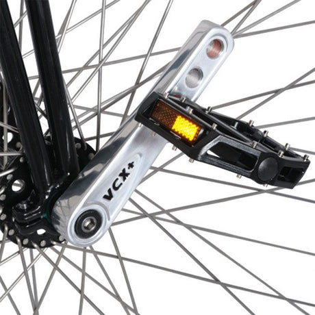 Närbild på den polerade Nimbus VCX Plus-vevarmen och svart pedal på höghjulingens framhjul, visar tydligt VCX+-märkningen