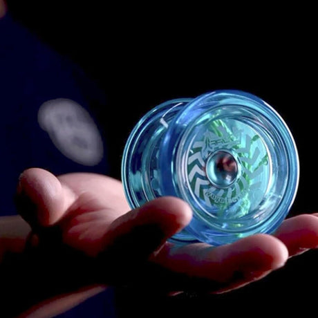 Närbild på en person som håller en genomskinlig blå Arrow jojo från YoyoFactory i handflatan. Jojon har vit grafik med pilar i ett cirkulärt mönster och ett grönt snöre syns inuti
