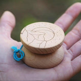 Närbild på en Boho Wooden jojo i ljust trä som ligger i en handflata. Jojons sida har en ingraverad design föreställande berg, en måne och små prickar som stjärnor. Ett blått snöre är knutet vid jojon.