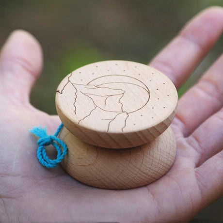 Närbild på en Boho Wooden jojo i ljust trä som ligger i en handflata. Jojons sida har en ingraverad design föreställande berg, en måne och små prickar som stjärnor. Ett blått snöre är knutet vid jojon.