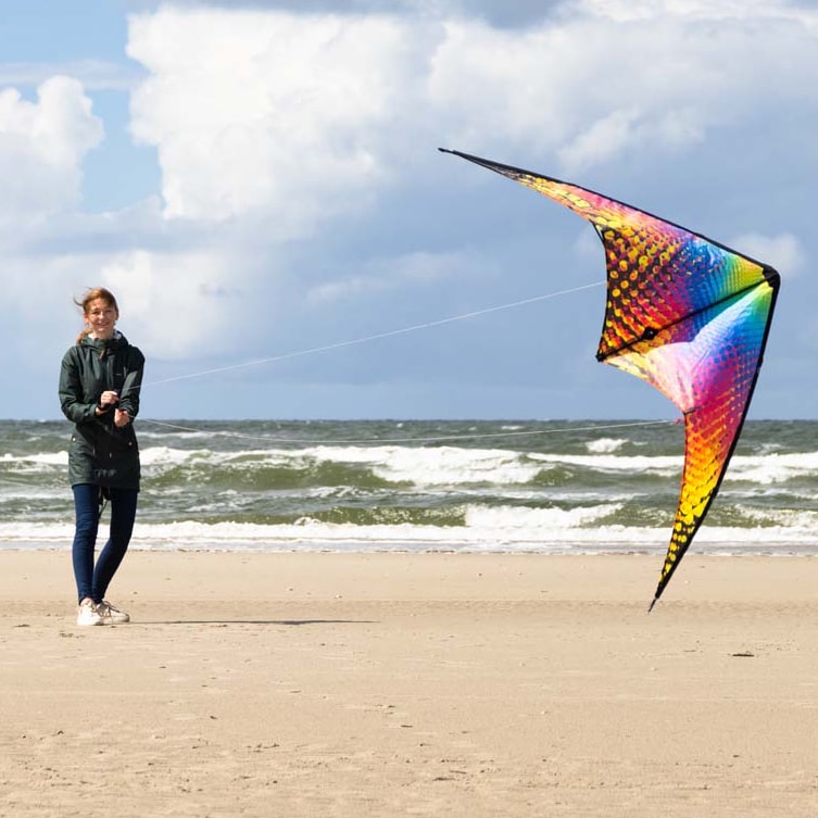 En kvinna som flyger en färgstark, mönstrad styrbar drake på en sandstrand vid havet.