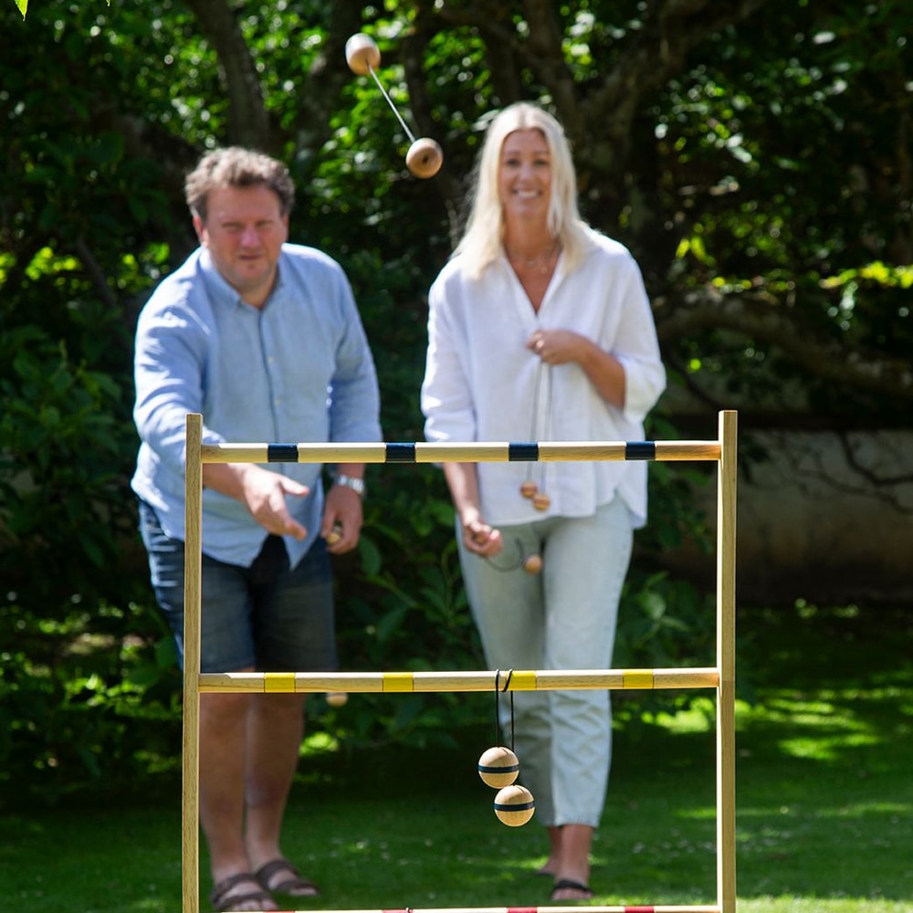 Två vuxna spelar Spin Ladder Original i trädgården – bollpar kastas mot stegen