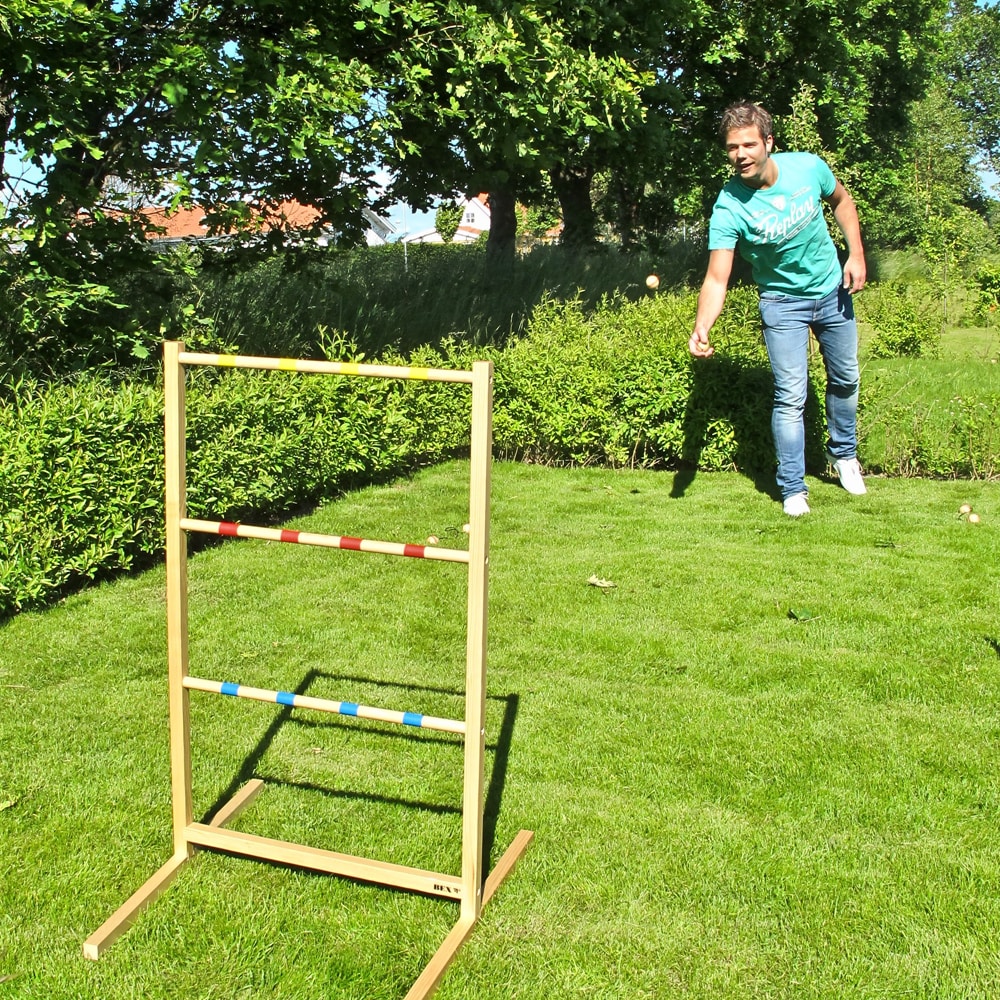 Två vuxna spelar Spin Ladder Original i trädgården – bollpar kastas mot stegen