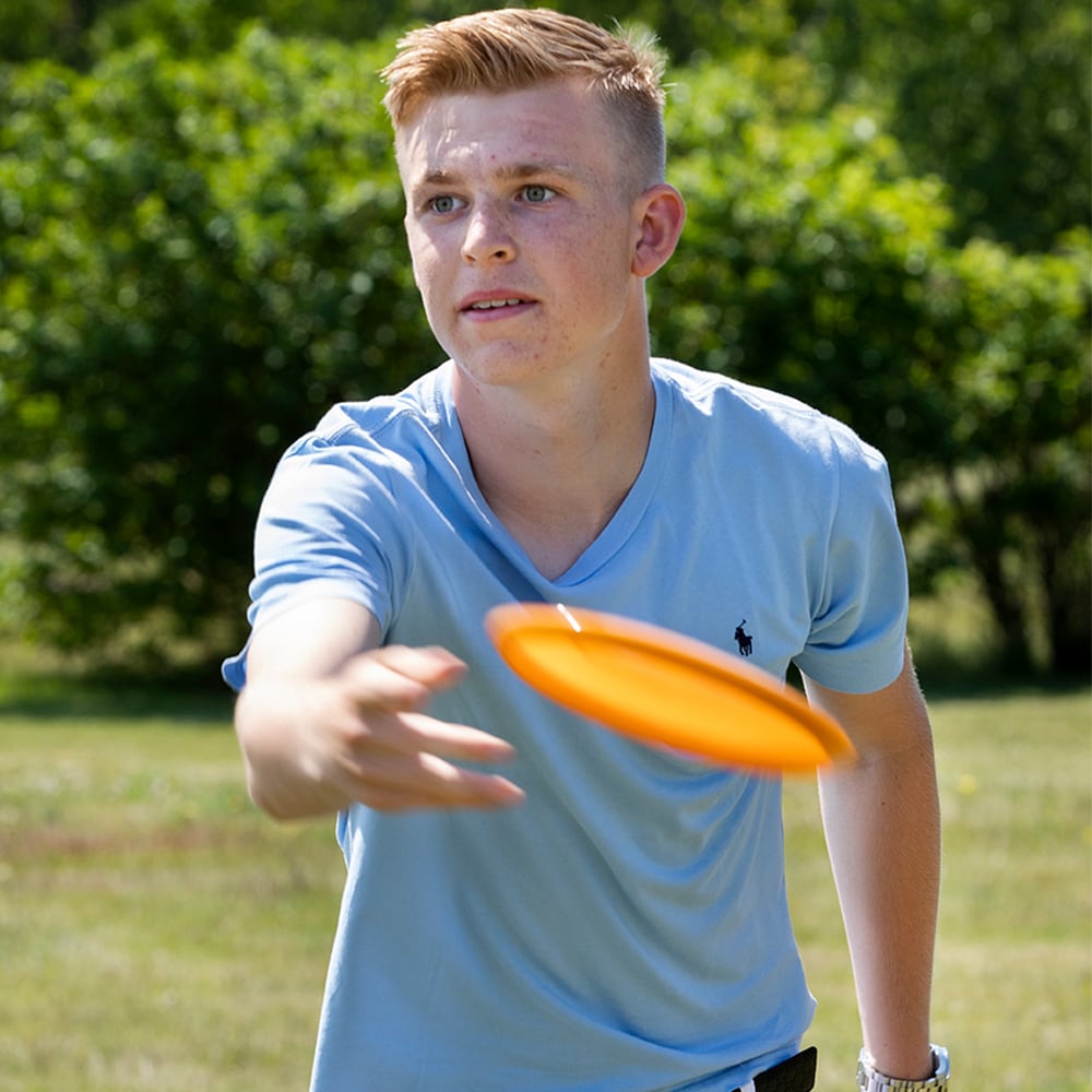 Person som kastar disc mot portabel discgolfkorg utomhus – perfekt för trädgård, park och nybörjare som vill träna discgolf hemma