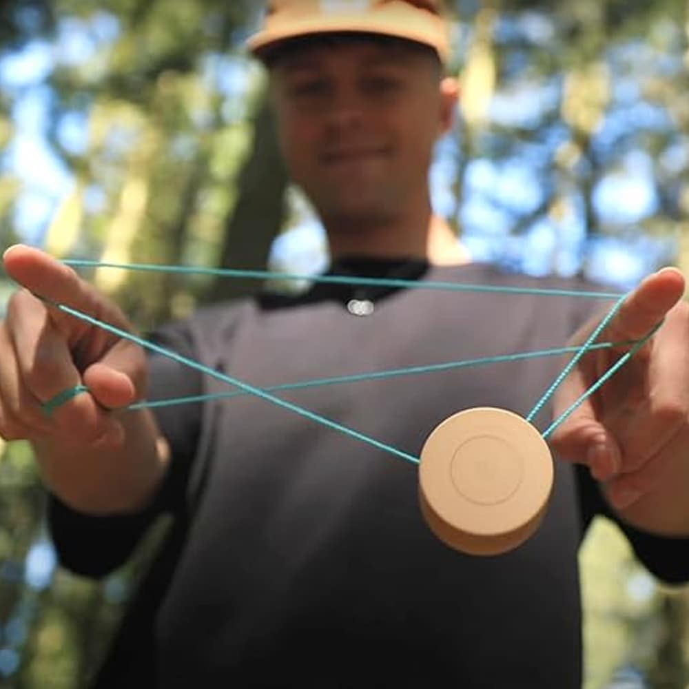 En person utför ett jojo-trick utomhus i en skog med en jojo i ljust trä. Ett turkost snöre är lindat runt personens fingrar och håller jojon i luften.